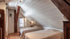 A room with two beds, wooden flooring, a sloped ceiling, and a small bedside table with a lamp. - Apartment 'L'Ancolie' with Mountain View, Shared Terrace and Wi-Fi (Saint-Ferréol)