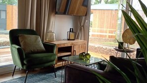 A modern living room with a green armchair, a dark sofa, a wooden coffee table, and a TV mounted on the wall. - Tidy Chalet With Dishwasher, 9 km From Maastricht (Berg en Terblijt)