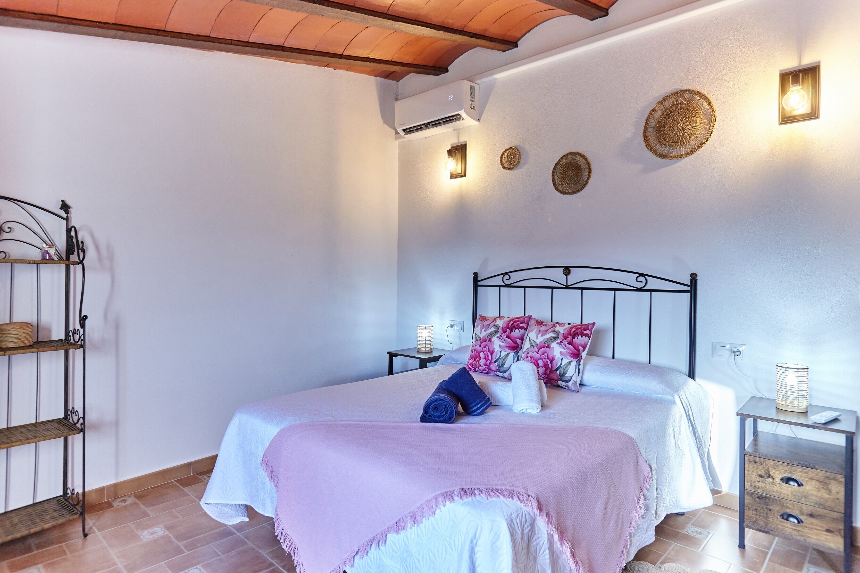 Un dormitorio con cama, mesitas de noche, aire acondicionado de pared y un estante con cestas.
