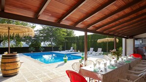 Een buitenzwembadgedeelte met een overdekt terras, ligbedden en een eettafel gedekt voor een maaltijd.