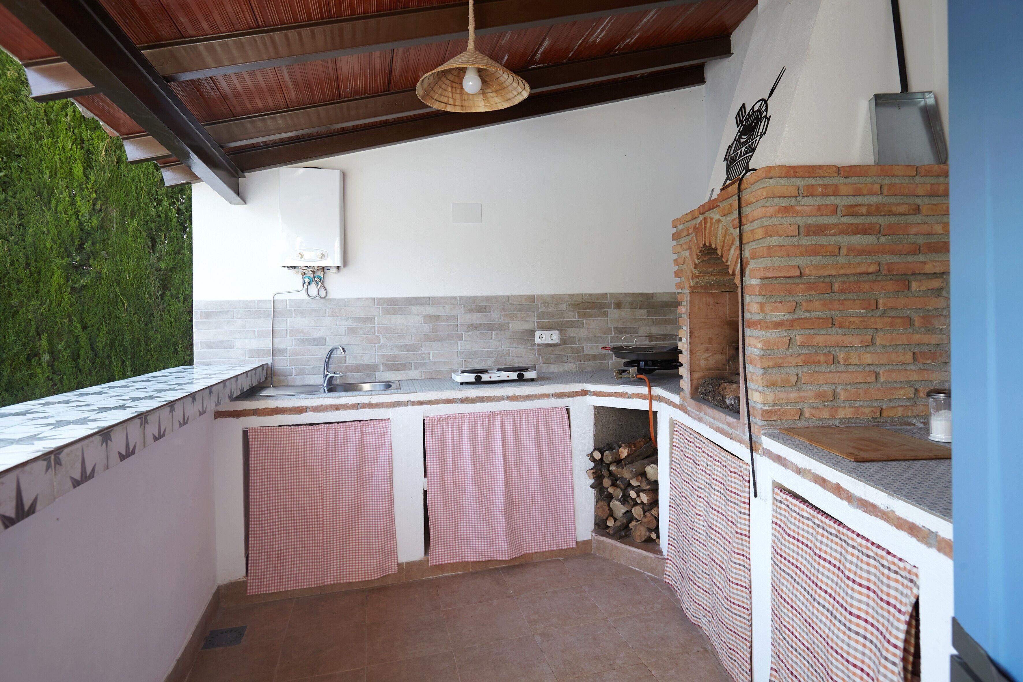 Cocina exterior con horno de ladrillo, estufa a gas y lámpara colgante.