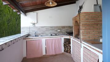 Cocina exterior con horno de ladrillo, estufa a gas y lámpara colgante.