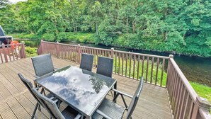 A deck with a table and chairs overlooking a river, surrounded by lush greenery. - 3 bedroom accommodation in Dollar (Dollar)
