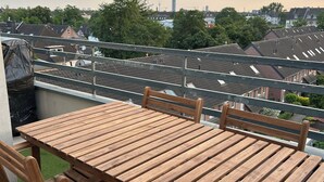 Una mesa y sillas de madera en un balcón con vista a una zona residencial y un edificio alto a lo lejos.