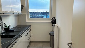 Una cocina moderna con ventana, armarios blancos, encimera negra y cubo de basura de acero inoxidable.