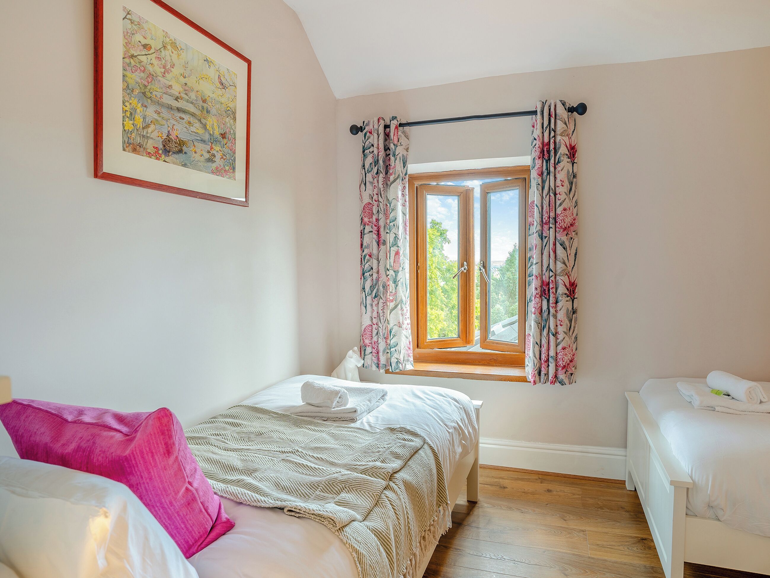 Un dormitorio con cama, ventana con cortinas, un cuadro en la pared y suelo de madera.