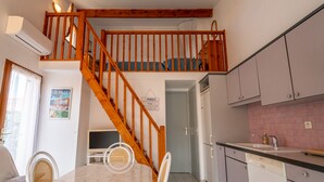 Ein zweistöckiges Haus mit einer Holztreppe, einem Essbereich mit einem Marmortisch sowie einer Küche mit Schränken und einem Spülbecken.