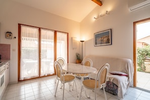 A dining area with a round table, white chairs, and a covered sofa. - Villa Gruissan Seaside- Les Ayguades (Gruissan)