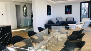 Una sala de estar moderna con una mesa de comedor de vidrio, sillas negras, un sofá y un amplio ventanal con vistas.