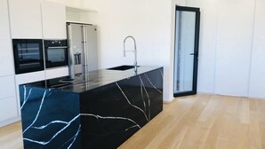 Una cocina moderna con una isla de mármol negro, electrodomésticos de acero inoxidable y una puerta de cristal que da a otra habitación.
