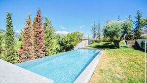 Una piscina rectangular con agua azul cristalina, rodeada de césped y varios árboles.