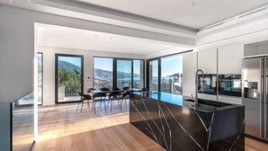 Cocina moderna con una isla de mármol negro, ventanas amplias con vista a la ciudad y un comedor con sillas.