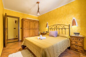 A bedroom with a bed, wooden wardrobe, bedside table, lamp, and a door leading to another room.