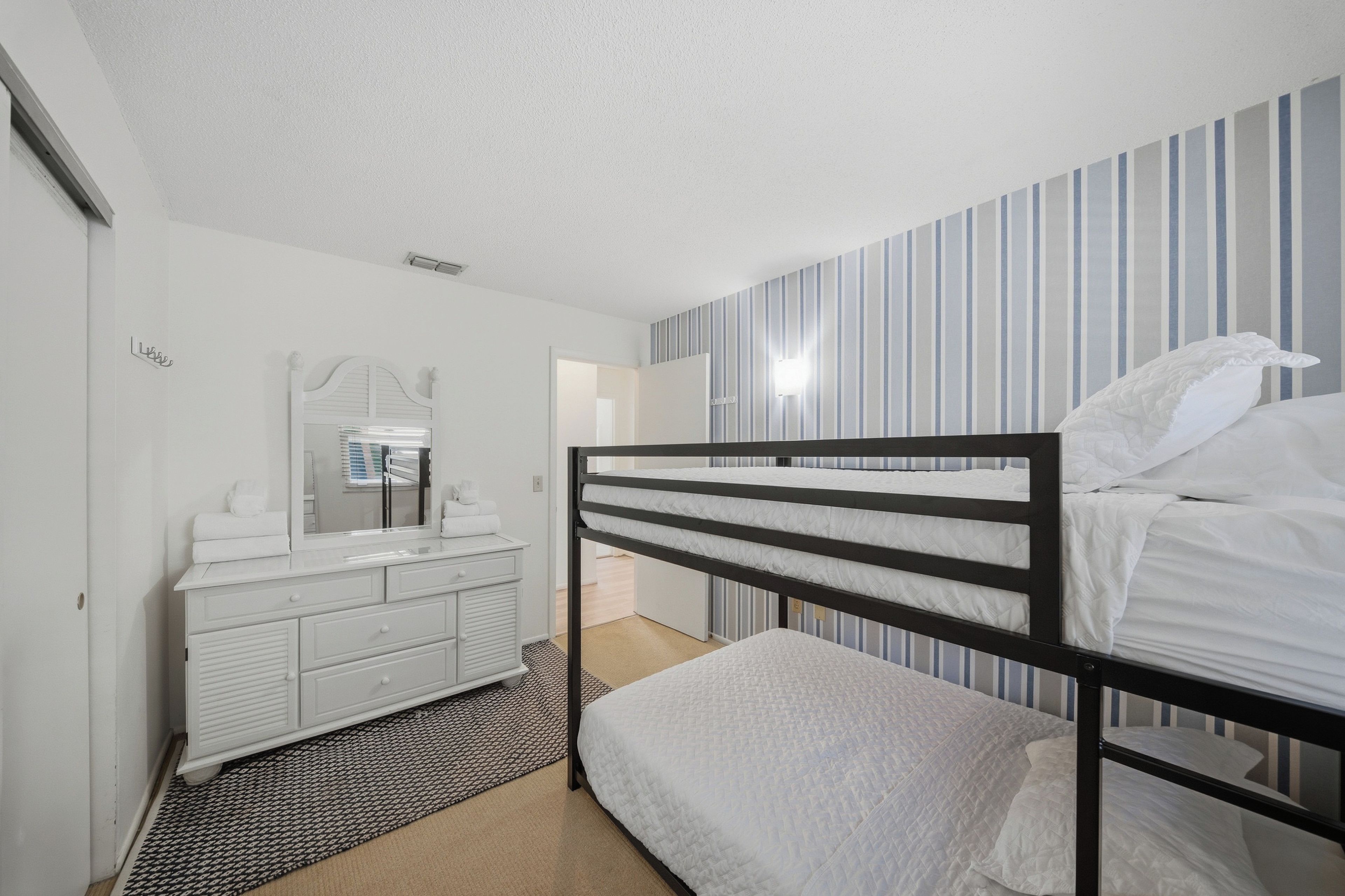 A bedroom with a bunk bed, a bedside table, a mirror, and a dresser.