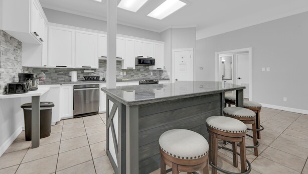 A modern kitchen with white cabinets, a large island, and bar stools. - Spacious & Central Pool Home By McAuliffe Park (McAllen)