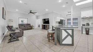 A spacious living area with a sofa, a TV, and a kitchen area with a bar. - Spacious & Central Pool Home By McAuliffe Park (McAllen)