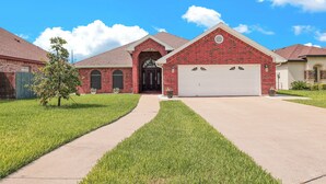A residential house with a brick facade, a white garage door, and a well-maintained lawn. - Spacious & Central Pool Home By McAuliffe Park (McAllen)