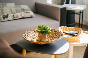 Un salon avec une table ronde, un panier en osier contenant une plante, une télécommande et un canapé avec des coussins.