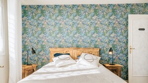 A bed with a wooden headboard, two bedside tables with lamps, and a floral wallpaper. - Holiday Home 'Maison Chaleureuse Cancale' with Private Terrace and Garden (Cancale)