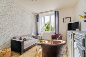 Un salon avec un canapé, deux fauteuils, un téléviseur et une fenêtre avec des rideaux.