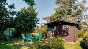A small wooden cabin with a sloped roof, surrounded by lush greenery and a few outdoor chairs. - Holiday Home 'Maison Chaleureuse Cancale' with Private Terrace and Garden (Cancale)