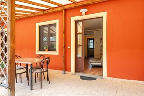 An outdoor patio with a table and chairs, a wooden pergola, and a door leading to an interior space. - Holiday Home 'Ortensia Verde' with Shared Pool, Wi-Fi and Air Conditioning (montecarlo)
