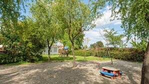 A gravel playground with a swing set, a picnic table, and a small shed in a garden. - Holiday Home 'Ortensia Verde' with Shared Pool, Wi-Fi and Air Conditioning (montecarlo)