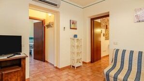 A living room with a television, a sofa, a white shelving unit, and a door leading to another room. - Holiday Home 'Ortensia Verde' with Shared Pool, Wi-Fi and Air Conditioning (montecarlo)