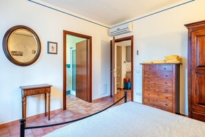 Een kamer met een bed, een houten dressoir, een spiegel en een deur naar een andere kamer.