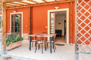 Een terras buiten met een houten tafel en stoelen, een bloempot en een houten pergola.