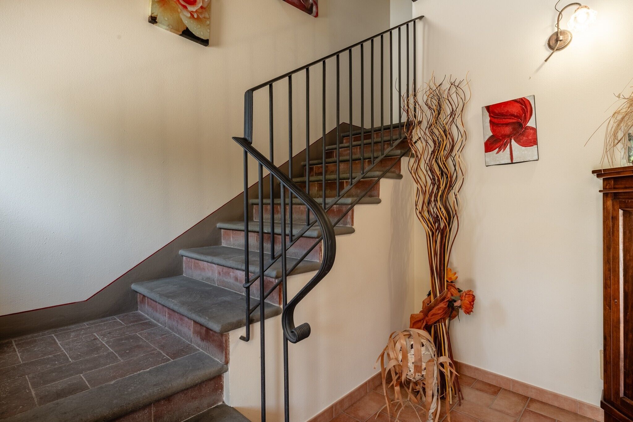 Un escalier avec une rampe en métal noir, un luminaire fixé au mur et une œuvre d’art encadrée.