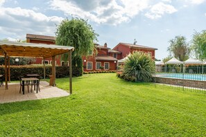 Un cortile con piscina, zona salotto coperta e un edificio dalla facciata rossa.