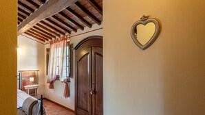 Une pièce comprenant un lit, une armoire en bois, un miroir et une fenêtre avec des rideaux.