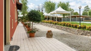 Un chemin mène à un bâtiment à la façade rouge, avec un espace extérieur couvert doté d’une piscine et des plantes en pot le long du sentier.