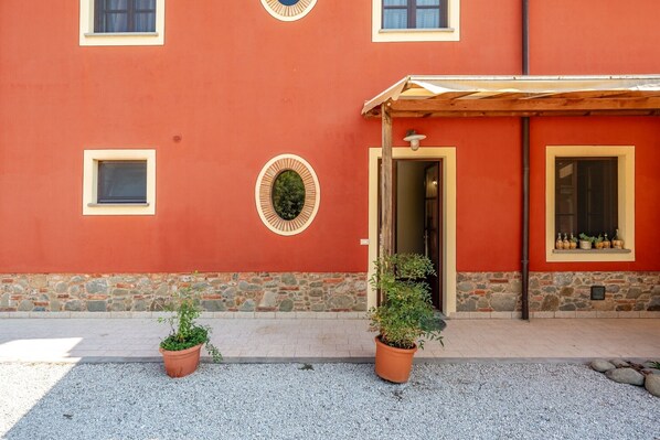 A building with a red facade, stone base, two potted plants, and a wooden pergola.