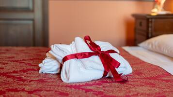 A neatly folded set of white towels tied with a red ribbon on a bed with a red patterned bedspread.
