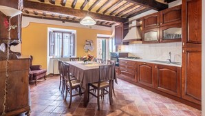 A rustic kitchen with wooden cabinets, a tiled floor, and a dining area with chairs and a table. - Room 'Camera Rossa' with Shared Terrace and Wi-Fi (Montalcino)