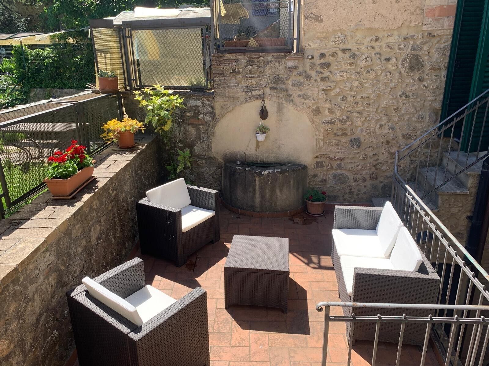 An outdoor patio with wicker furniture, a stone wall, and a metal railing.