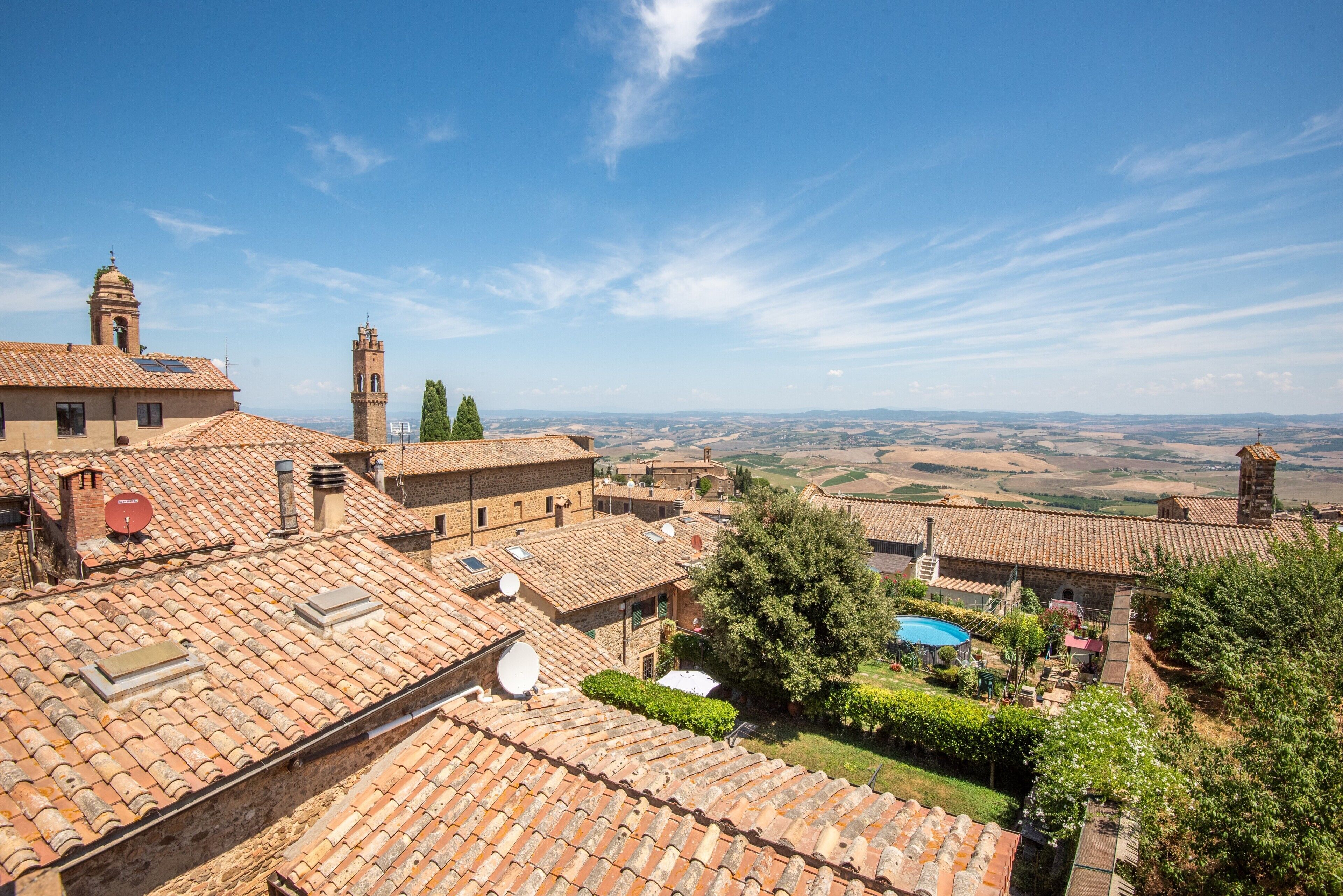 A village with terracotta-roofed buildings, a prominent church tower, and a clear blue sky.
