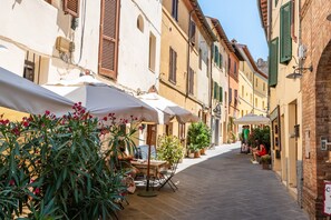 Una calle estrecha con mesas al aire libre, plantas en macetas y edificios tradicionales.