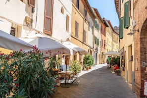A narrow street with outdoor seating, potted plants, and traditional buildings. - Room 'Camera Beige' - Beb del Musico with Private Terrace, Balcony and Wi-Fi (Montalcino)