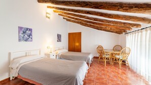 A room with two beds, a wooden ceiling, a dining table with chairs, and a door.