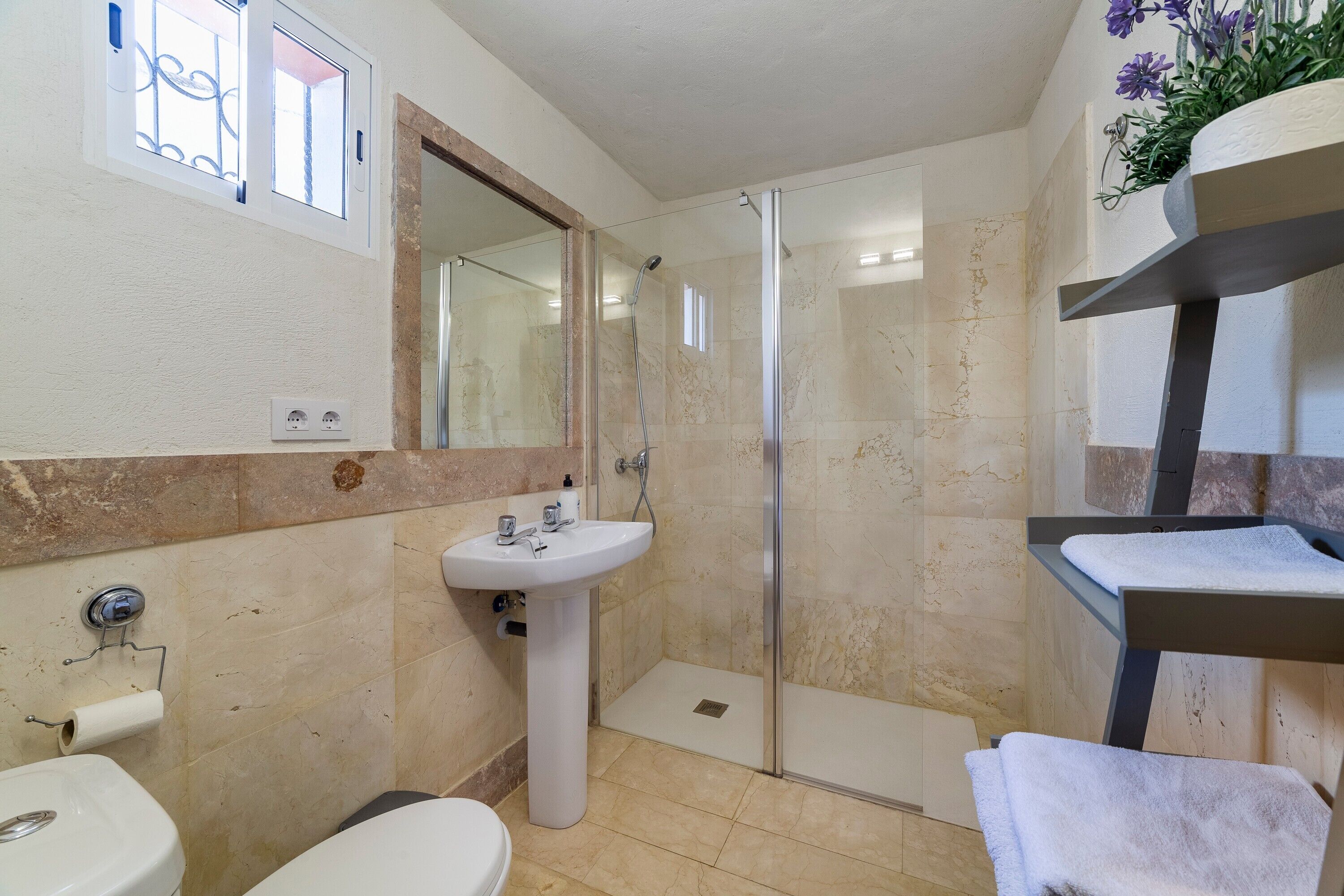 Un baño con lavamanos pedestal, inodoro, ducha con mampara de vidrio y toallero.