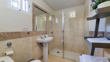 Un baño con lavamanos pedestal, inodoro, ducha con mampara de vidrio y toallero.