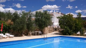 A swimming pool with lounge chairs, a stone wall, and a building in the background.