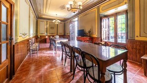 A spacious dining area with a long table and chairs, a chandelier, and a television.