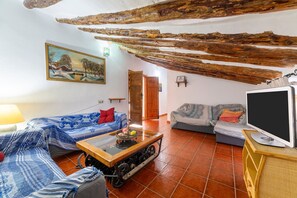 Ein rustikaler Raum mit Holzbalkendecke, einem Gemälde, einem Sofa, einem Fernseher und einem Tisch mit einer Dekoration.
