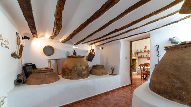 A rustic interior with exposed wooden beams, large clay pots, and a tiled floor.