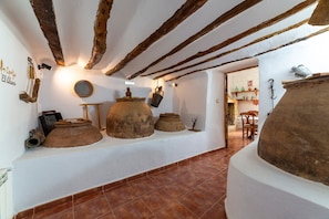 Ein rustikales Interieur mit freiliegenden Holzbalken, großen Tongefäßen und einem gefliesten Boden.