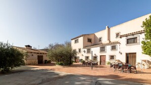 A courtyard with a building featuring a tiled roof, multiple windows with bars, and outdoor seating.